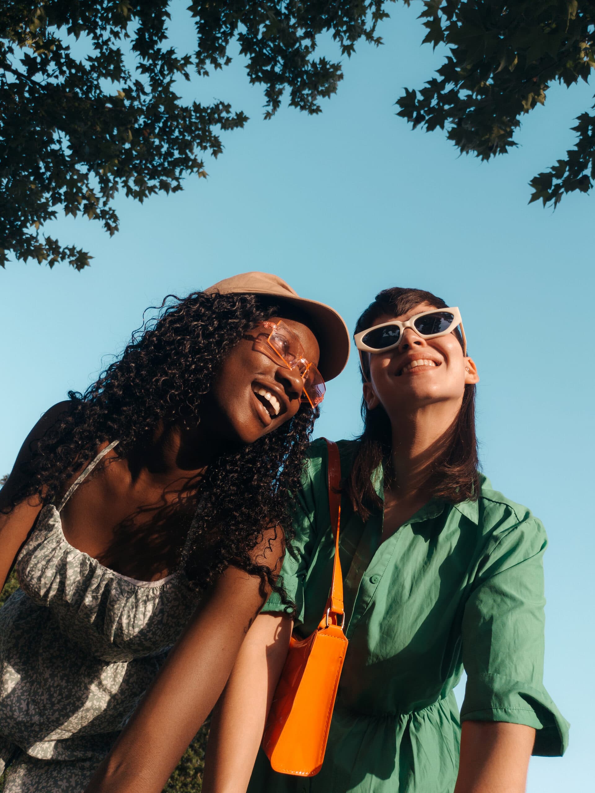 Two cool and happy multiracial women friends, smiling and laughing outdoors with sunglasses