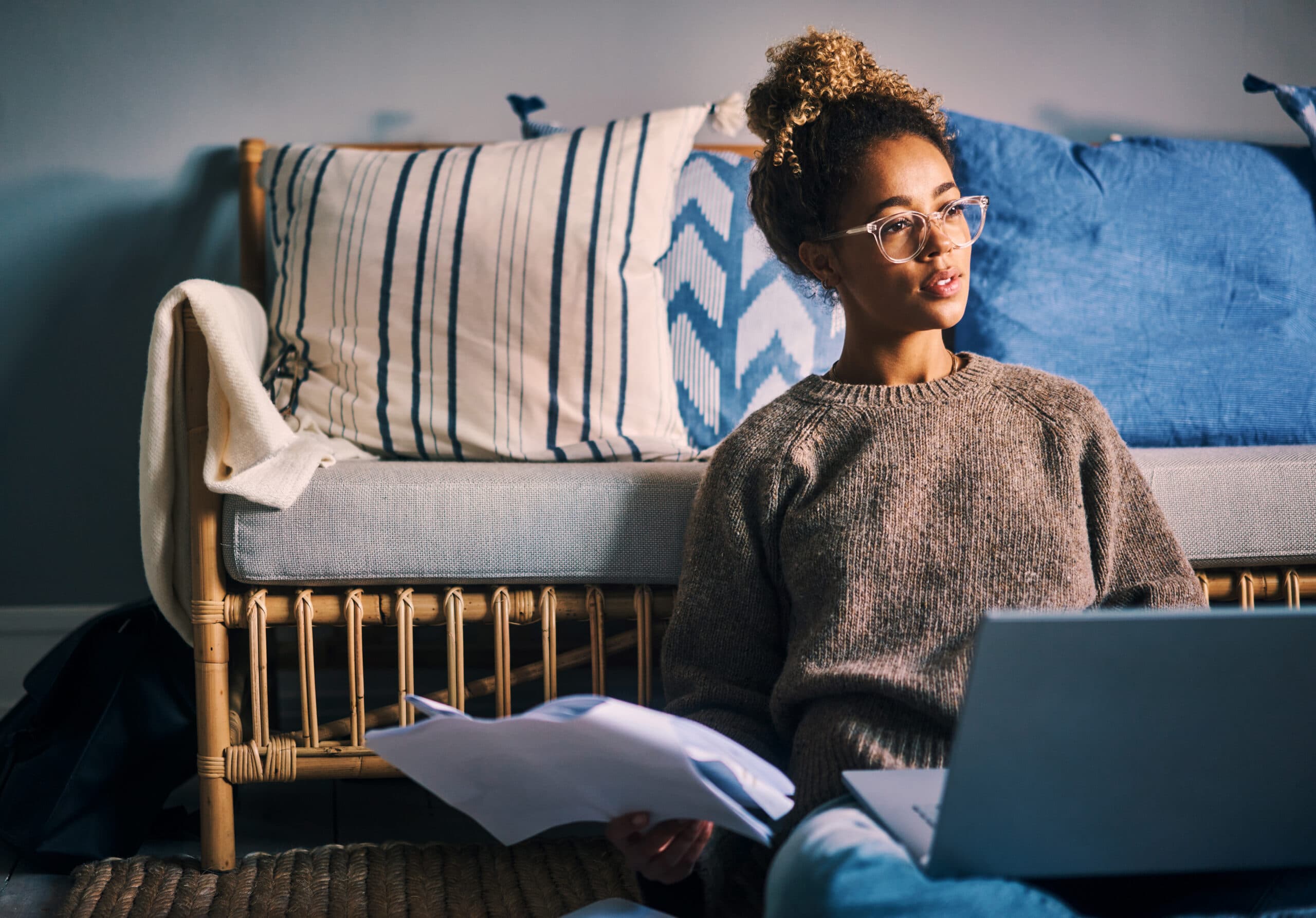 Shot of a young woman going through paperwork while using a laptop at home